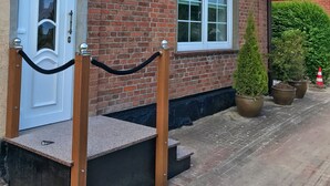 A brick building with a white door, a window, and a small staircase leading to the entrance. - Hochzeitsberg - Double room / Apartment "Tromsö" in Breege (Breege)