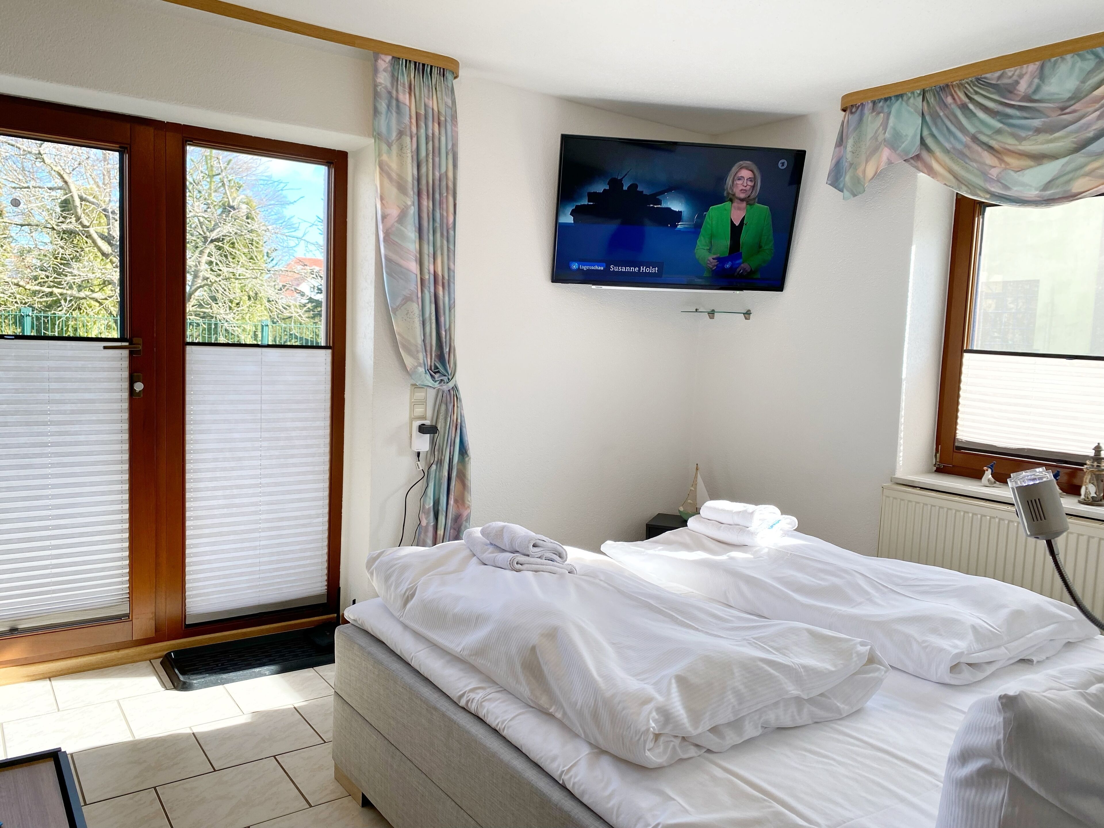Hotellihuone, jossa on sänky, seinälle asennettu televisio ja ikkuna, jossa on verhot.