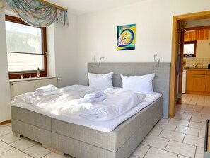A neatly made bed with white linens and towels, a grey headboard, and a colorful abstract painting on the wall. - Apartments Stadtmitte - Apartment 3 (Sassnitz)