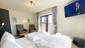 A hotel room with a bed, two chairs, a TV, and a window with curtains. - Apartments Stadtmitte - Apartment 3 (Sassnitz)
