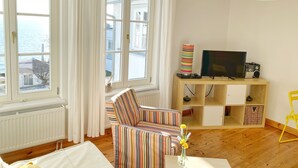 A living room with a striped sofa, a TV on a wooden stand, a radiator, and a view of the sea through large windows. - Seaside Appartements, "yellow" (Sassnitz)
