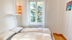 A bedroom with a bed, pillows, a window, and a wall-mounted lamp. - Seaside Appartements, "yellow" (Sassnitz)