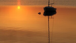 Un voilier est amarré près d’un coucher de soleil sur des eaux calmes.