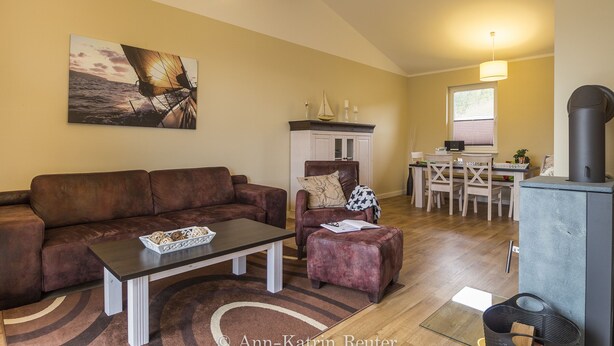 Un salon avec un canapé en cuir marron, une table basse et une cheminée. On y trouve également un coin repas avec une table et des chaises.