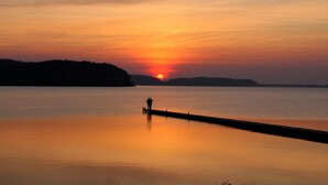 Un coucher de soleil sur un lac paisible, avec une jetée qui s’avance dans l’eau.