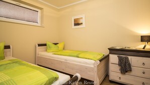 Une chambre avec deux lits, une commode, une fenêtre avec des stores et un tableau encadré au mur.