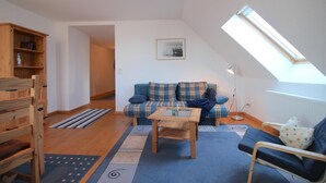 Ein gemütliches Wohnzimmer mit Schlafkoje, einer Couch, einem Couchtisch und einem Bücherregal.