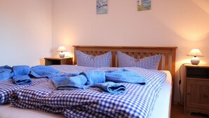 Ein ordentlich bezogenes Bett mit karierter Bettwäsche, zwei Nachttischlampen und einem hölzernen Kopfteil.