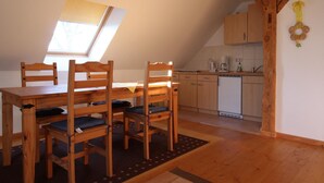 Una habitación acogedora con una mesa y sillas de madera, un pequeño rincón de cocina y un techo inclinado con tragaluz.