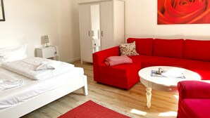 Un dormitorio moderno con una cama blanca, un sofá rojo, una mesita redonda y un armario.
