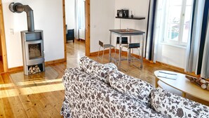 A modern living room with a wood-burning stove, a sofa, a dining table with chairs, and a view through a window. - Seaside Apartments, "Brown" (Sassnitz)