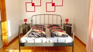 Une chambre à coucher avec un lit à ossature métallique, deux tables de chevet avec des lampes rouges et un plancher en bois.