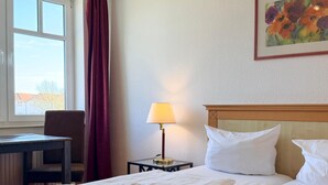 A hotel room with a bed, a desk, a lamp, and a painting on the wall. - Apartment 309 - Roundel at the Jasmundtherme (Neddesitz)