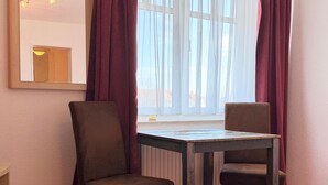A room with two chairs, a table, a bed, a window with curtains, and a mirror on the wall. - Apartment 309 - Roundel at the Jasmundtherme (Neddesitz)
