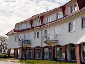 A multi-story building with a red-tiled roof, multiple balconies, and large glass doors.