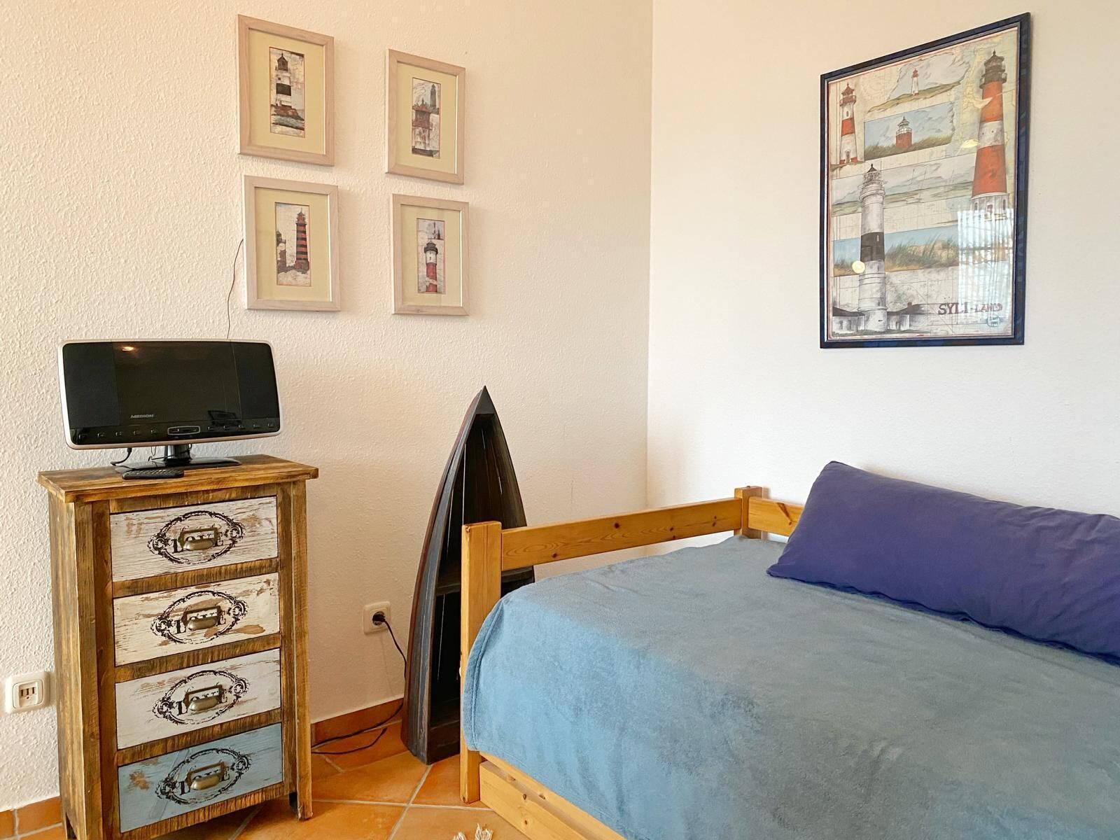 Een slaapkamer met een bed, een televisie op een houten dressoir en een lijst met foto’s van vuurtorens aan de muur.