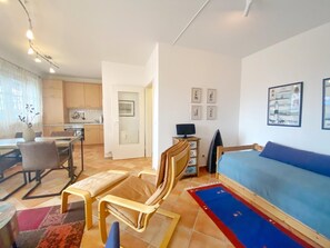 Um espaço de estar compacto com sofá, mesa de jantar com cadeiras, área de cozinha e televisão.