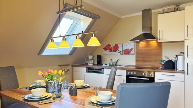 Une cuisine moderne avec un coin repas, dotée d’une verrière, de luminaires suspendus et offrant une vue sur le ciel.