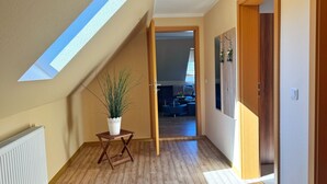 Un couloir avec une lucarne, un plancher en bois, une plante en pot et une vue sur un espace de vie.
