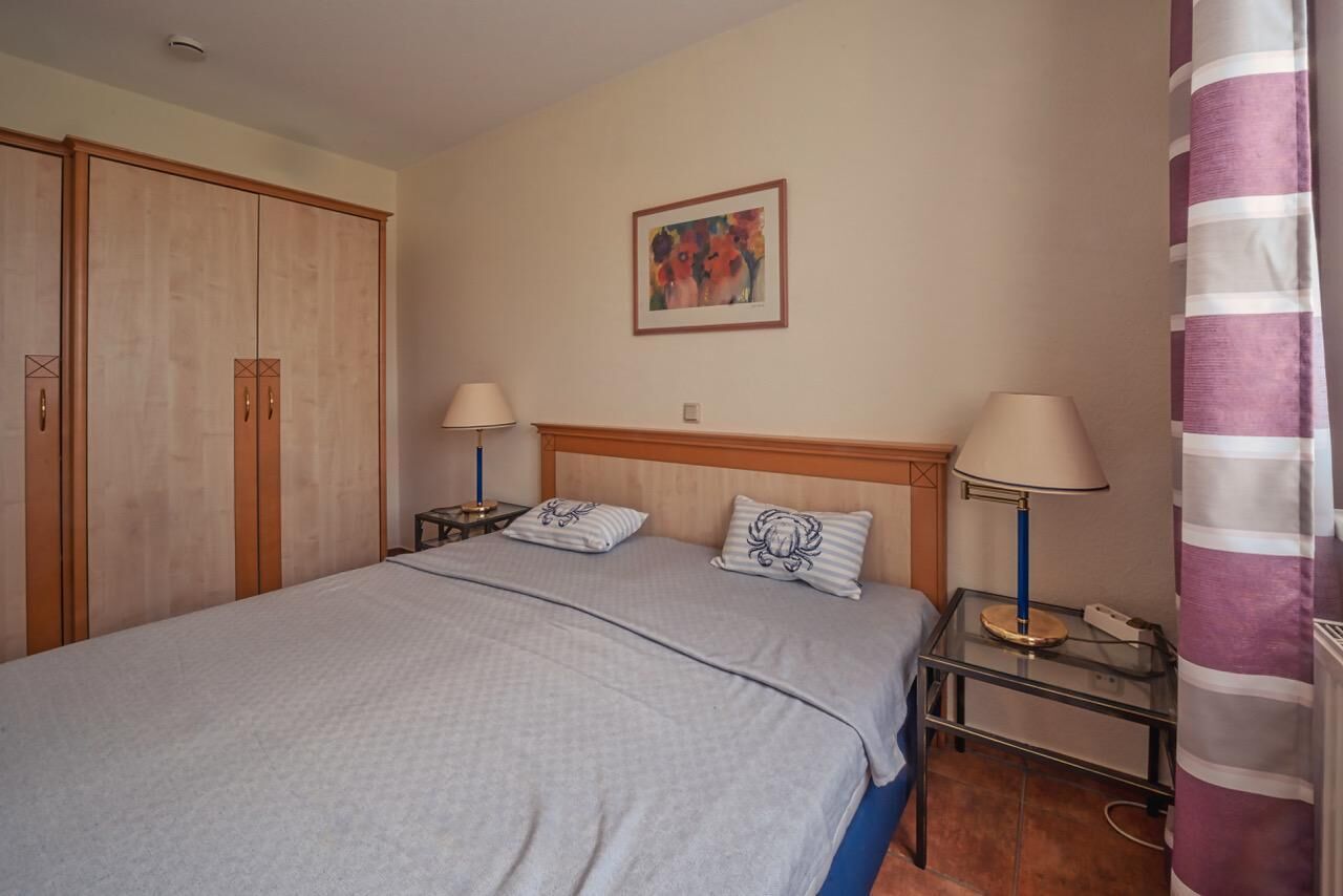 Ein Schlafzimmer mit einem Bett, zwei Nachttischen mit Lampen, einem Holzschrank und einem gerahmten Bild an der Wand.