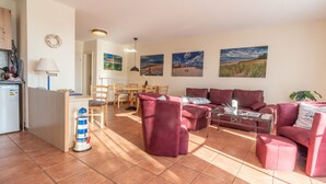 A living room with a red sofa set, a coffee table, and a dining area with wooden chairs and a table. - Vacation apartment Neddesitz No. 51 (Neddesitz)