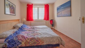 A bedroom with a bed, a window with red curtains, a radiator, and a painting on the wall. - Vacation apartment Neddesitz No. 51 (Neddesitz)