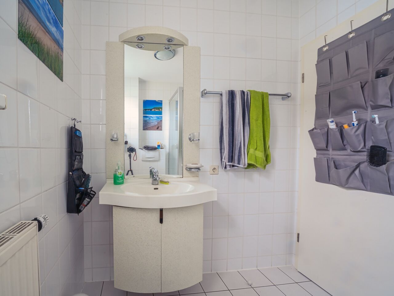 Ein Badezimmer mit weißem Waschbecken, Spiegel und Handtuchhalter. Ein Handtuch hängt am Halter, und es gibt einen Handtuchhalter mit mehreren Fächern.