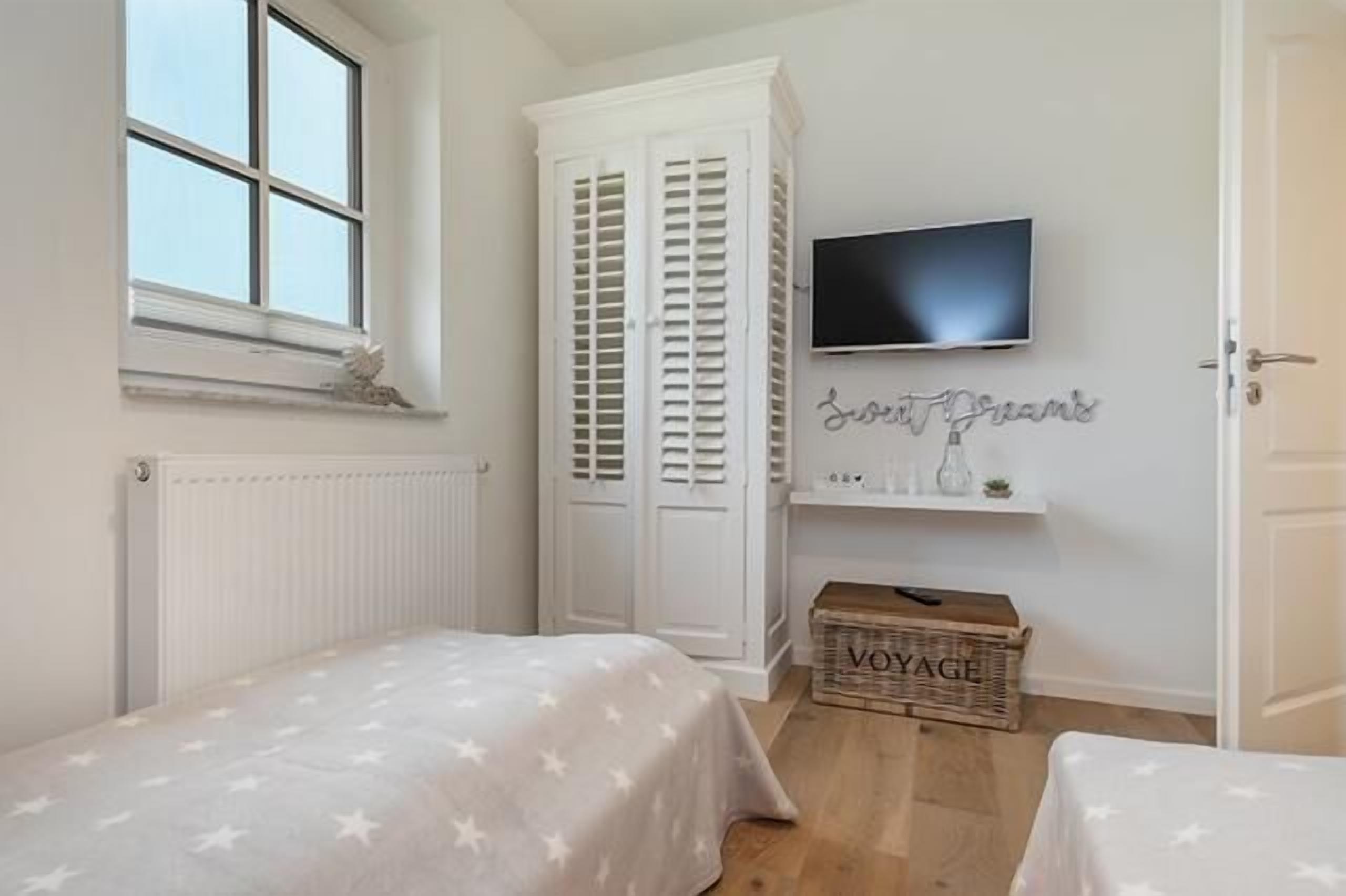 Un dormitorio con dos camas, un televisor, un armario y una pequeña estantería con adornos.