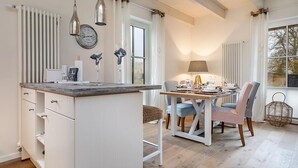 A modern kitchen with white cabinetry, a central island, pendant lighting, and a dining area with a table and chairs. - Semi-detached house Freyh II (Lohme OT Ranzow)