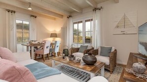 A cozy living room with a white sofa, a wooden coffee table, and a dining area with a lamp and chairs. - Semi-detached house Freyh II (Lohme OT Ranzow)