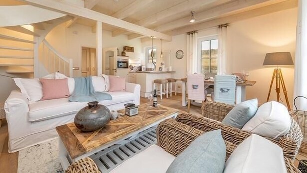 A spacious living area with a white sofa, a wooden coffee table, wicker furniture, and a kitchen in the background. - Semi-detached house Freyh II (Lohme OT Ranzow)