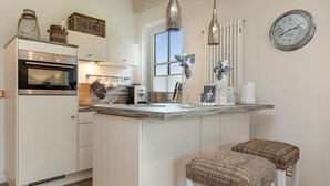 A modern kitchen with white cabinetry, a built-in oven, a stainless steel range hood, a window, and a clock on the wall. - Semi-detached house Freyh II (Lohme OT Ranzow)