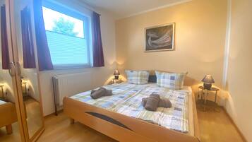 Un dormitorio con una cama de madera, una ventana con cortinas, un radiador, dos lámparas de noche y un cuadro en la pared.