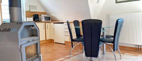 Una cocina moderna con estufa integrada, microondas y refrigerador. Hay dos sillas negras alrededor de una mesa pequeña.