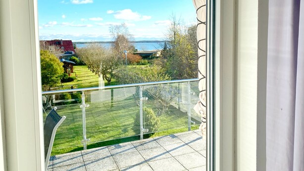 Un balcon offrant une vue dégagée sur une cour verdoyante, des arbres et une étendue d’eau au loin.