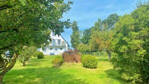 Une maison à l’extérieur blanc, entourée d’une pelouse bien entretenue et de divers arbres.