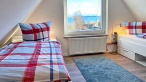 Une chambre avec deux lits, une grande fenêtre donnant sur un beau paysage, un radiateur et une table de chevet avec une lampe.