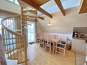 Eine geräumige Küche mit Essbereich, einer Holztreppe und großen Fenstern.