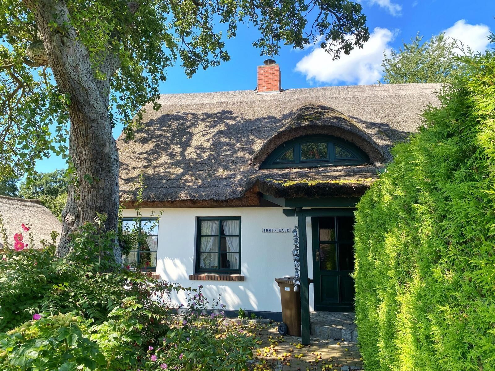 Ein traditionelles reetgedecktes Cottage mit weißer Fassade, einer grünen Tür und einem Schild mit der Aufschrift "IRMIS KATE".