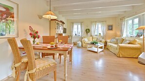 Een ruime woonkamer met een houten eettafel, rieten stoelen en een gele bank.