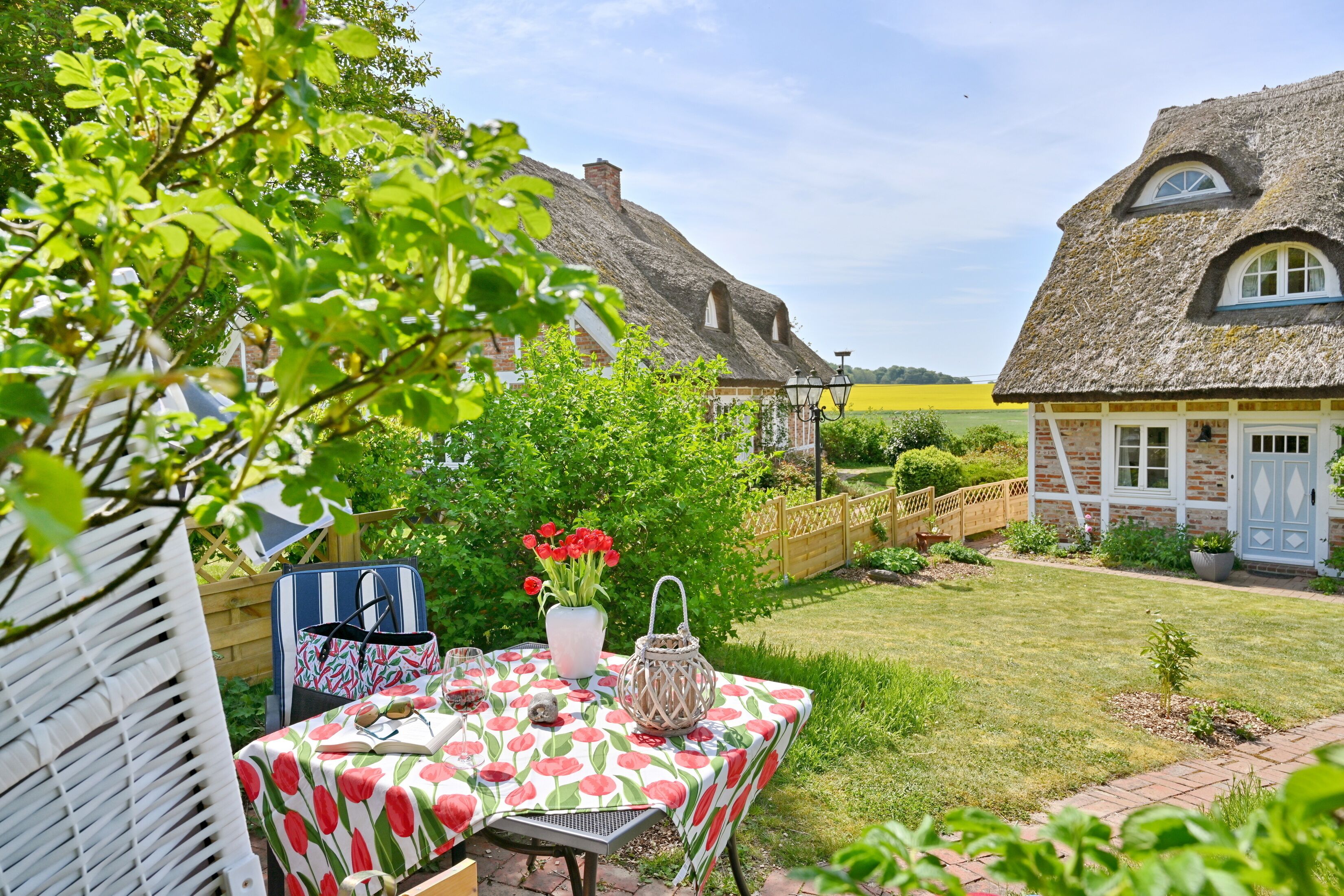 Un jardin avec une table dressée pour le repas, entouré de maisons aux toits de chaume.