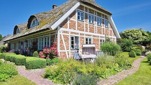 A traditional house with a thatched roof, brick walls, and a well-maintained garden with a pathway leading to the entrance. - Landhaus Vilmnitz, Wohnung 7 (Vilmnitz)