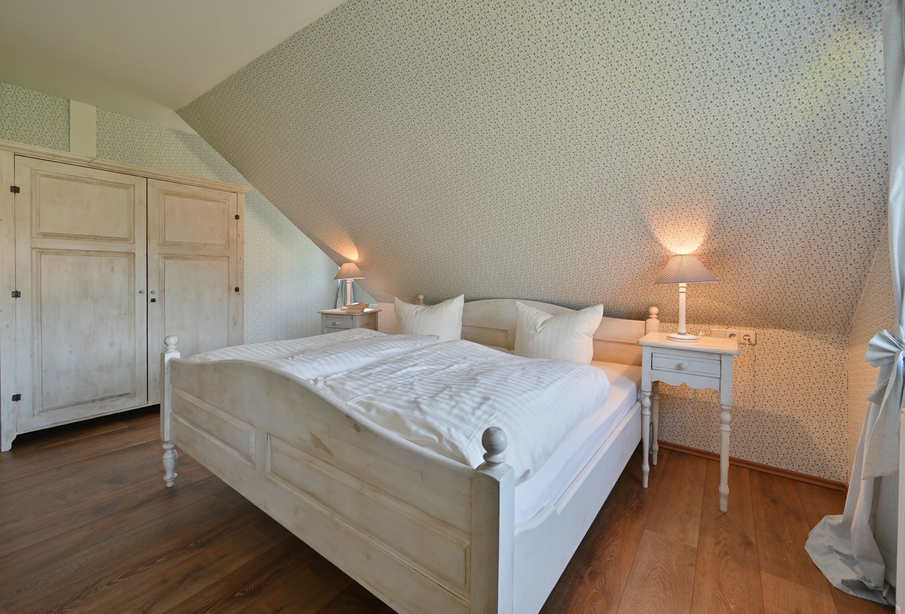 Ein Schlafzimmer mit einem hölzernen Bett, zwei Nachttischen mit Lampen, einem Kleiderschrank und einer geneigten Decke.