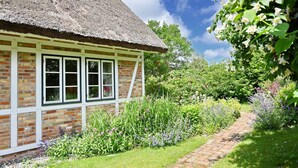 A traditional thatched-roof house with a brick exterior, surrounded by a well-maintained garden with various flowering plants and a brick pathway. - Landhaus Vilmnitz, Wohnung 8 (Vilmnitz)