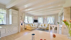 A spacious living room with a large table, a sofa, and a television. There are windows with curtains and a view of greenery outside. - Landhaus Vilmnitz, Wohnung 8 (Vilmnitz)