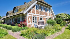 A traditional house with a thatched roof, brick walls, and a well-maintained garden with a pathway leading to the entrance. - Landhaus Vilmnitz, Wohnung 10 (Vilmnitz)
