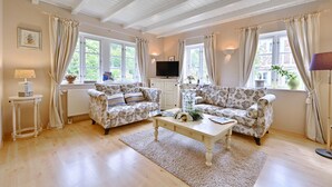 A cozy living room with two patterned sofas, a coffee table, a television, and a window with curtains. - Landhaus Vilmnitz, Wohnung 10 (Vilmnitz)
