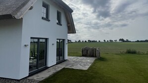 A modern house with a large glass door, a thatched roof, and a grassy yard. - Ferienhaus "rugard" mit Panoramasauna und Boddenblick (Dranske)