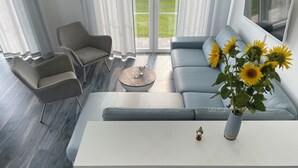 A modern living room with a sofa, chairs, a coffee table, and a vase with sunflowers. - Ferienhaus "rugard" mit Panoramasauna und Boddenblick (Dranske)