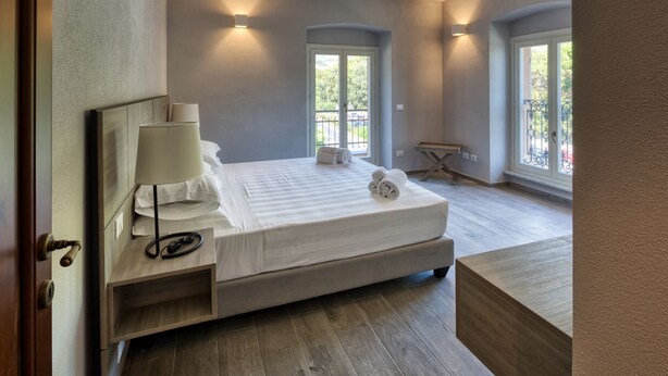 Ein Schlafzimmer mit einem Bett, einem Nachttisch, einer Lampe und zwei Fenstern.